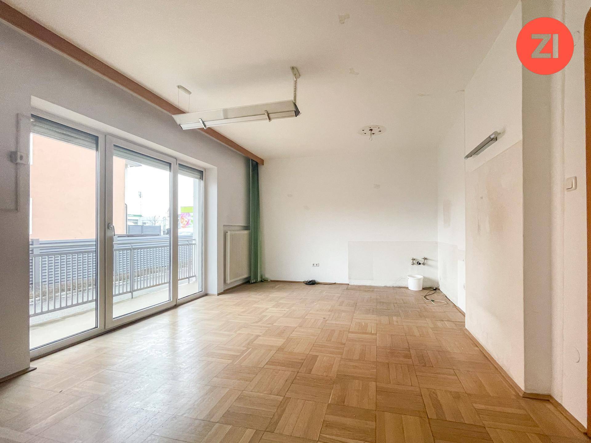 Heller Raum mit Parkettboden und großem Fenster, das Zugang zu einem Balkon bietet.