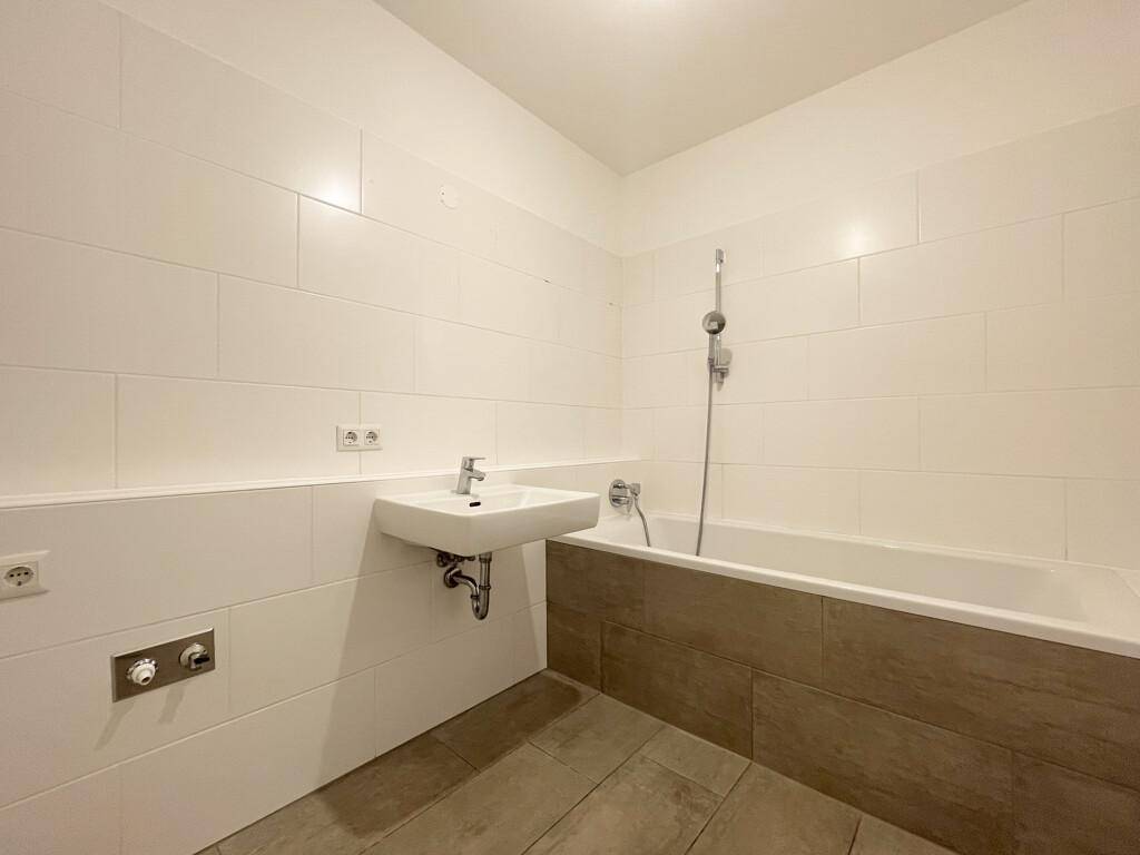Modernes Badezimmer mit Badewanne, weiß gefliesten Wänden und einem einzelnen Waschbecken.
