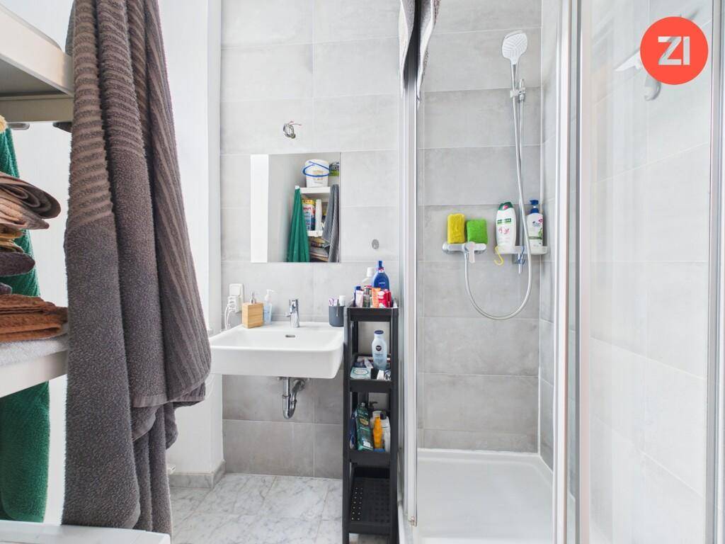 Modernes Badezimmer mit Duschkabine, Waschbecken und hellen Fliesen an Wänden und Boden.