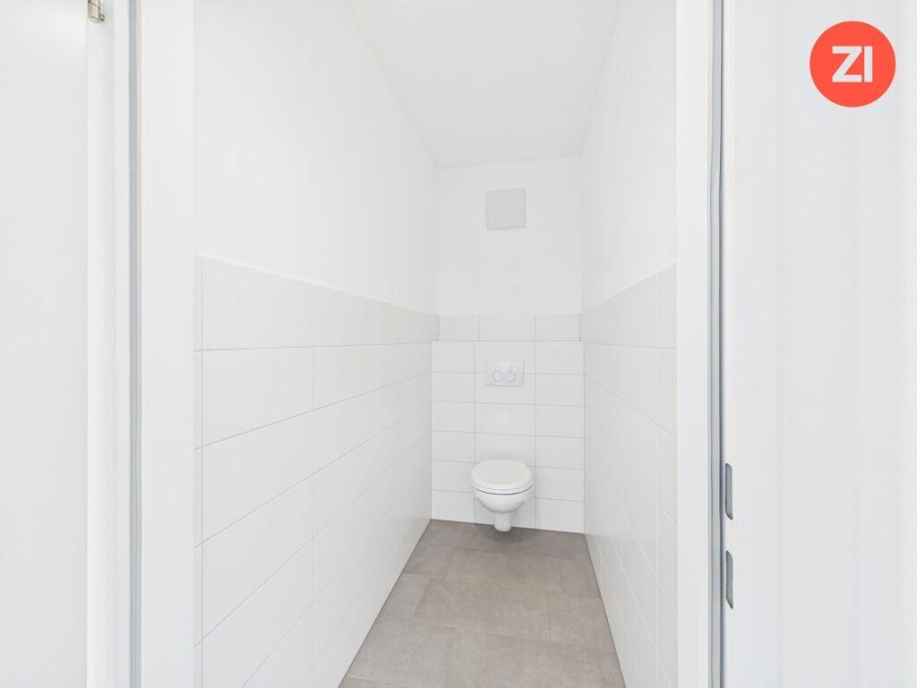 Separates WC mit wandhängender Toilette und modernen Fliesen, in schlichtem Design gehalten.