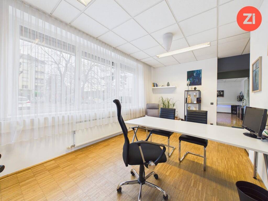 Geräumiges Büro mit Holzboden, Schreibtisch, Bürostühlen und großen Fenstern mit Vorhängen.