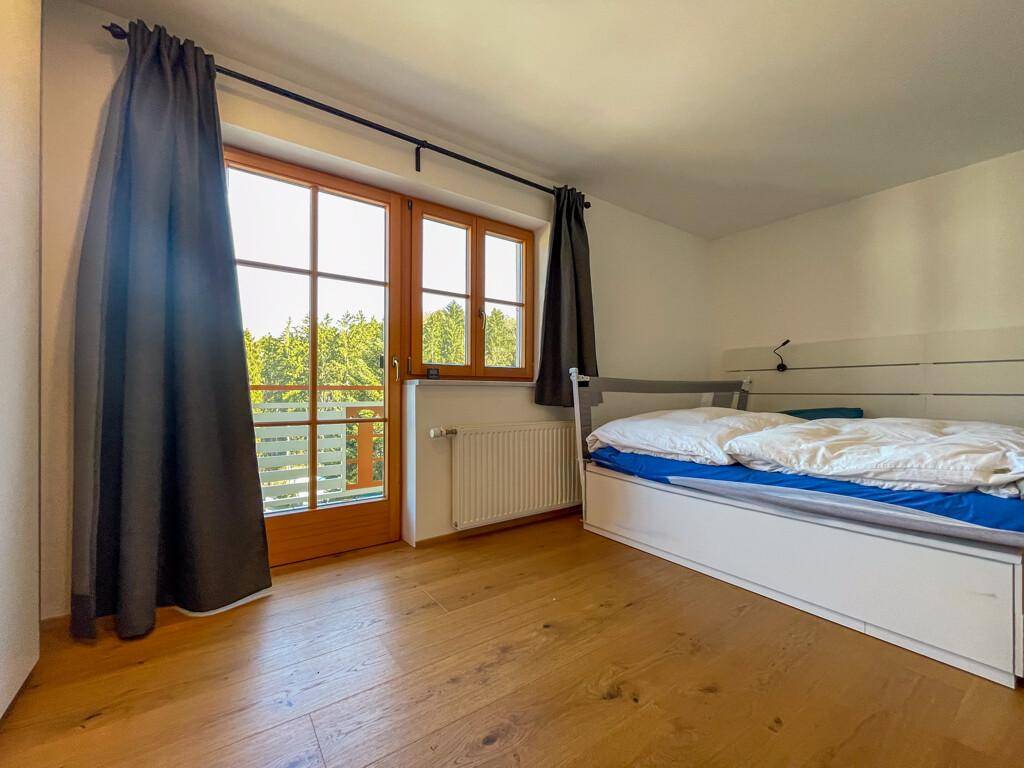 Helles Schlafzimmer mit Holzboden, Bett und Zugang zu einem französischen Balkon.