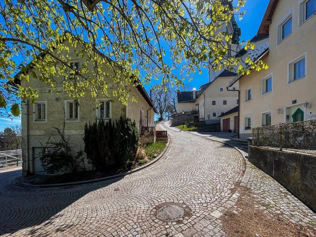 Eine gepflasterte Straße führt bergauf, gesäumt von traditionellen Gebäuden und frischem Frühlingsgrün.