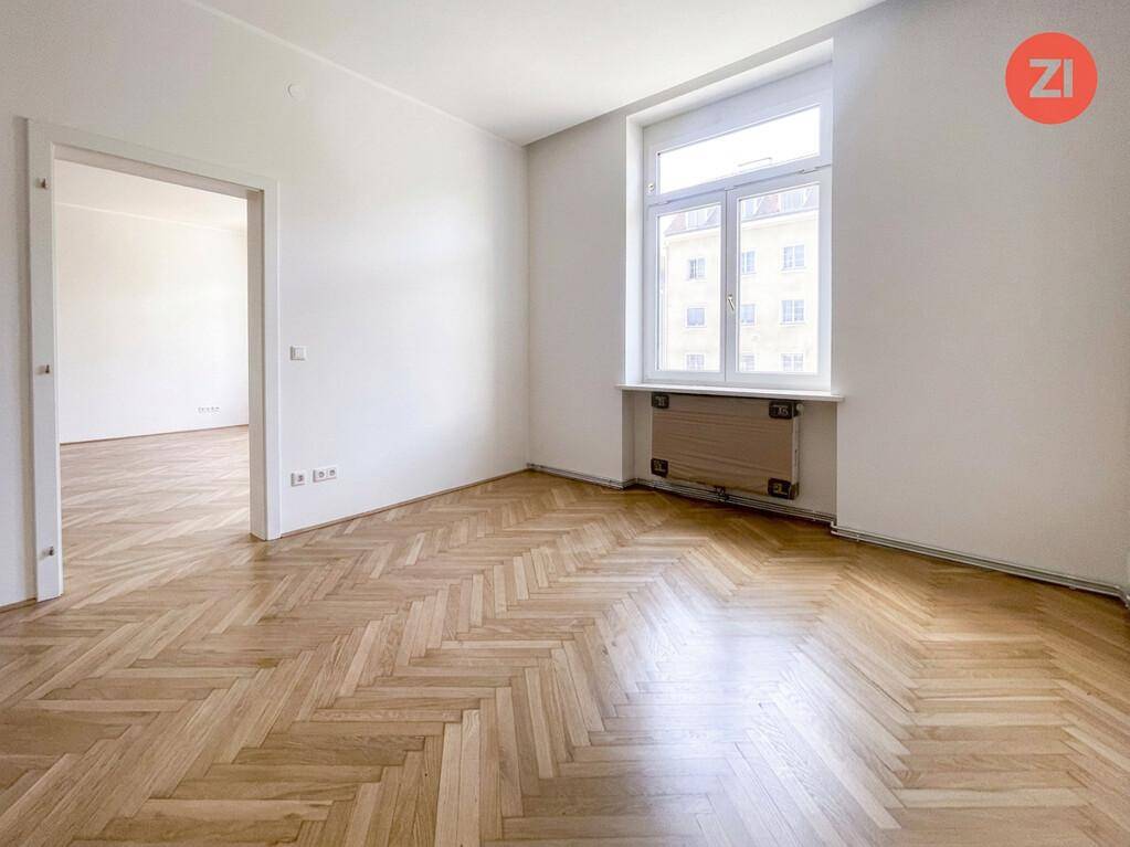 Helles Zimmer mit elegantem Fischgrätparkettboden und einem großen Fenster, das viel Licht hereinlässt.