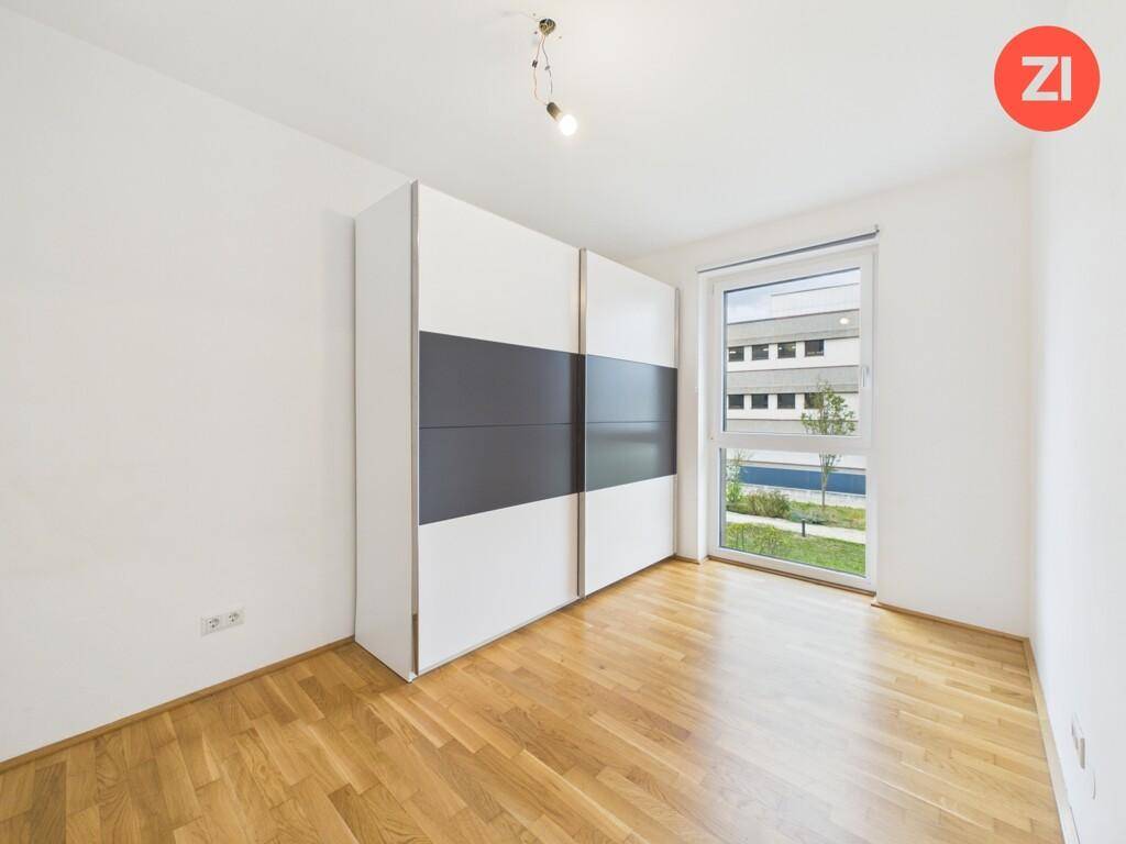Schlafzimmer mit großem Fenster, Parkettboden und einem modernen Schiebetürenschrank.