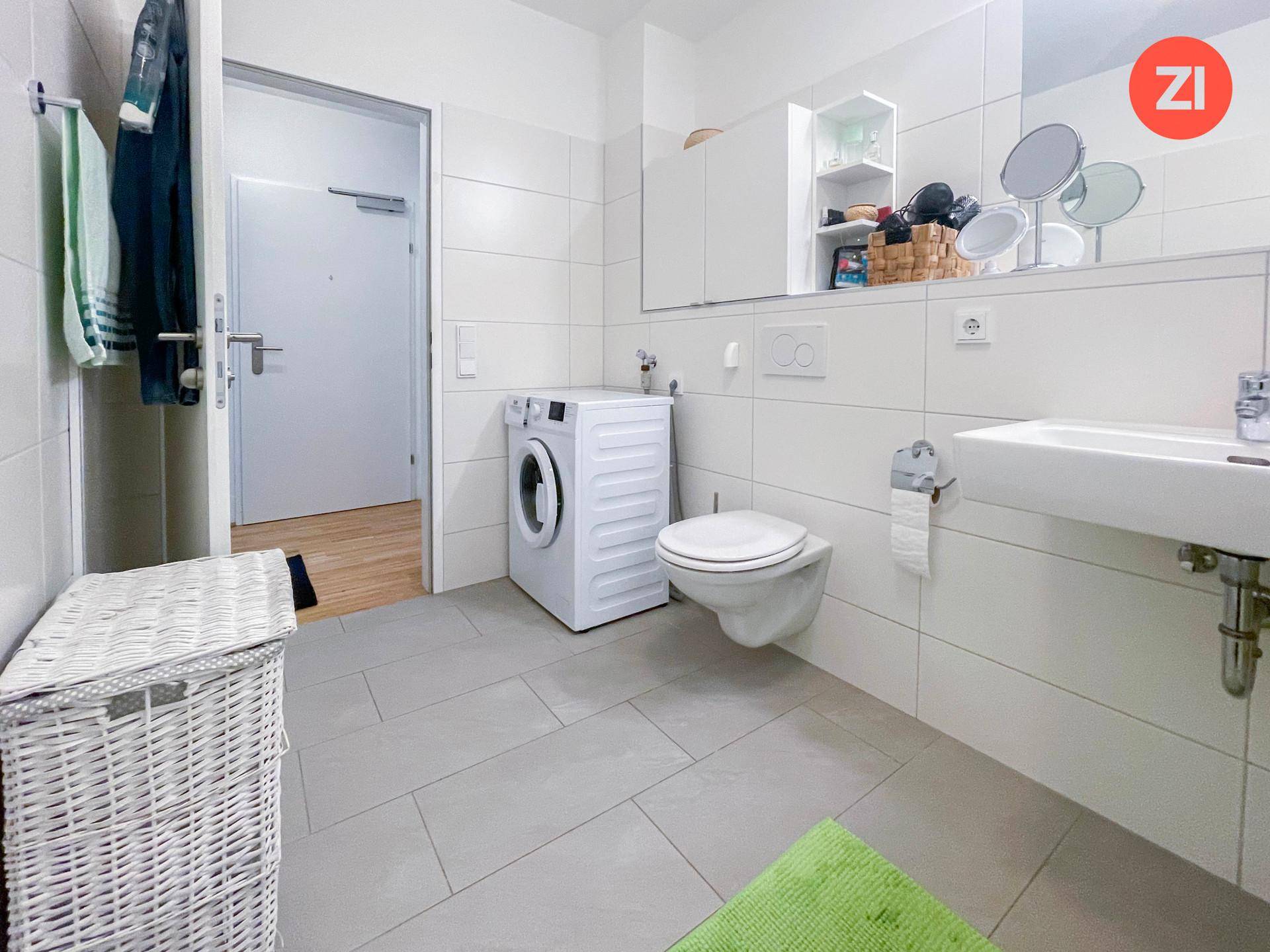 Funktionales Badezimmer mit Waschmaschine, WC und Waschbecken, hell gefliest.