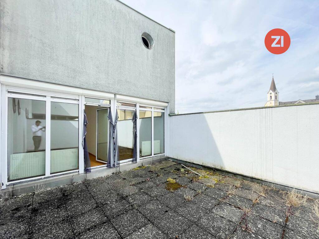 Große Dachterrasse mit Betonplatten und Blick auf eine Kirchturmspitze, bietet Potenzial für Gestaltung.