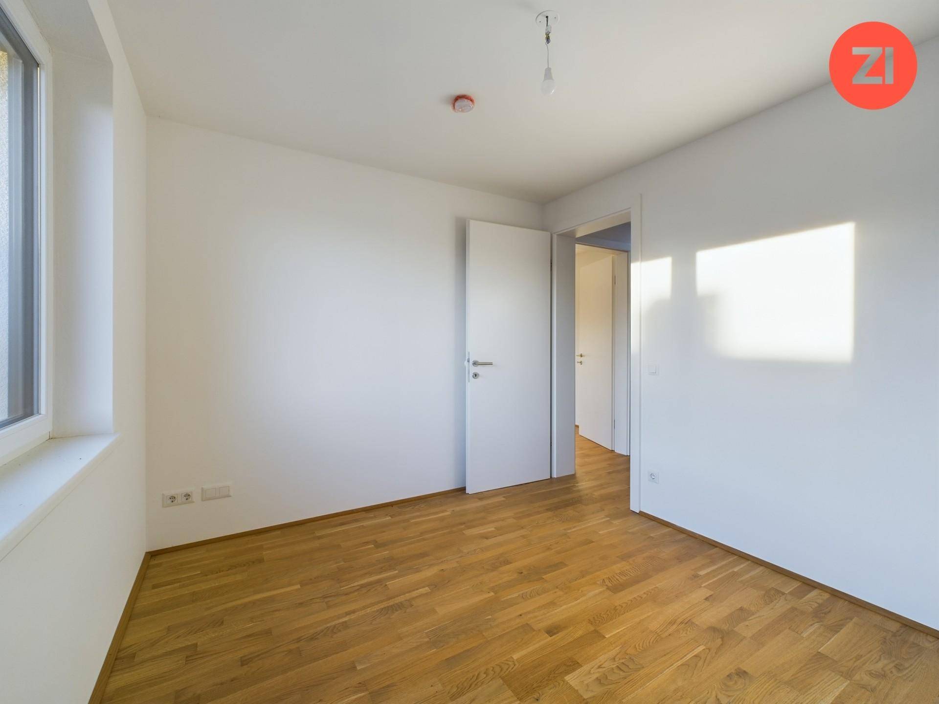 Leeres Schlafzimmer mit Holzboden und einem Fenster, das viel Tageslicht hereinlässt.