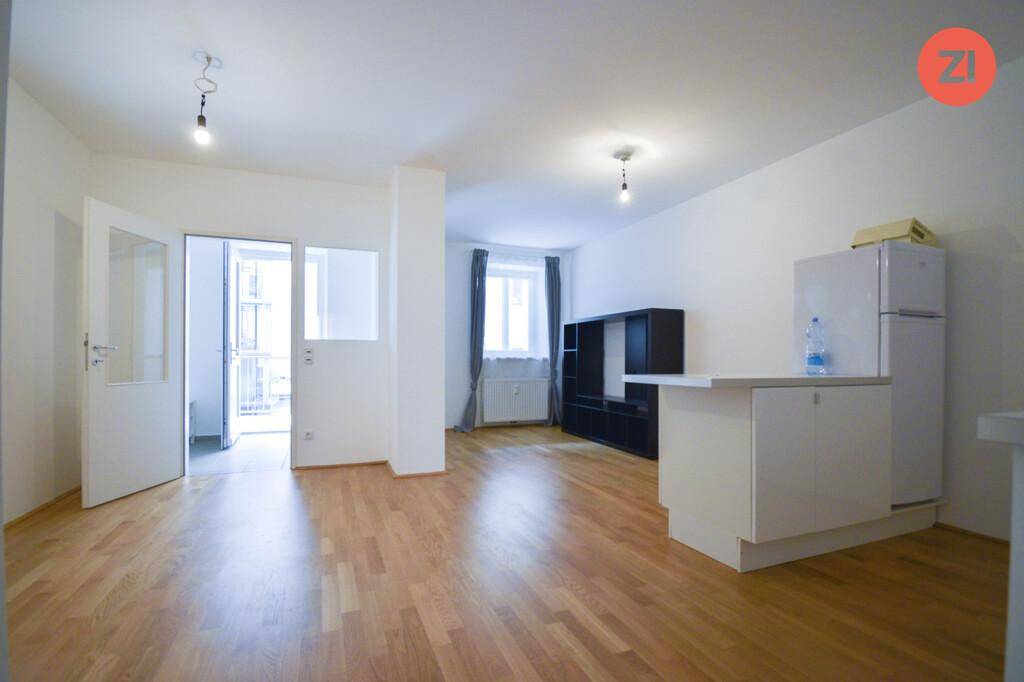 Heller Wohnbereich mit Zugang zum Balkon, Parkettboden und einer kleinen Küchenzeile.
