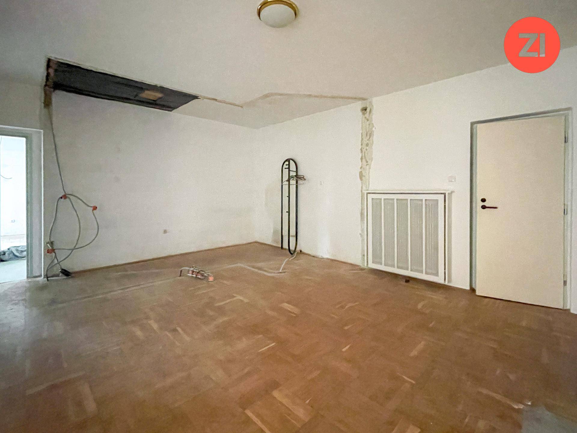 Leerer Raum mit Parkettboden und Heizkörper, der auf Renovierung wartet.