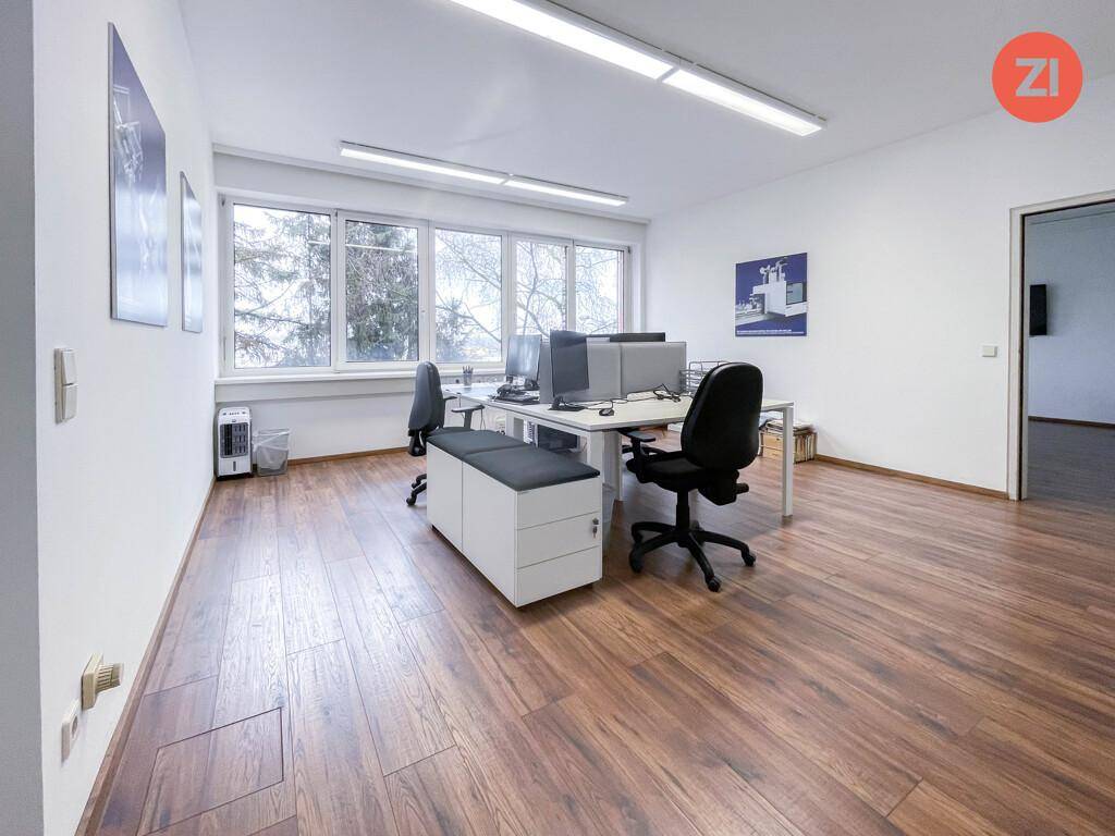 Modern eingerichtetes Büro mit mehreren Schreibtischen, Laminatboden und großen Fenstern mit Ausblick.
