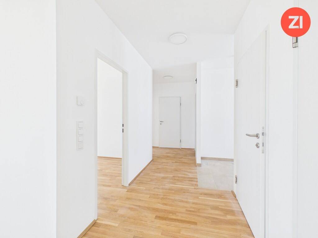 Heller Flur mit Holzboden, der zu verschiedenen Räumen und einem gefliesten Bereich führt.