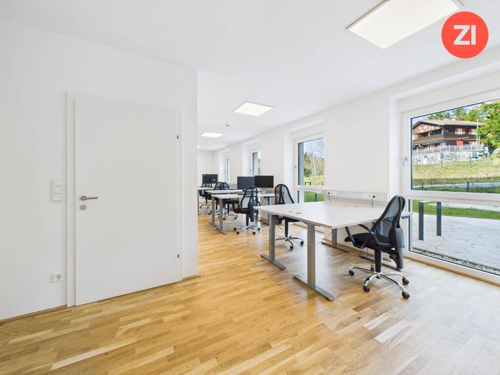 Helles Büro mit mehreren Arbeitsplätzen, Parkettboden und großen Fenstern mit Blick ins Grüne.