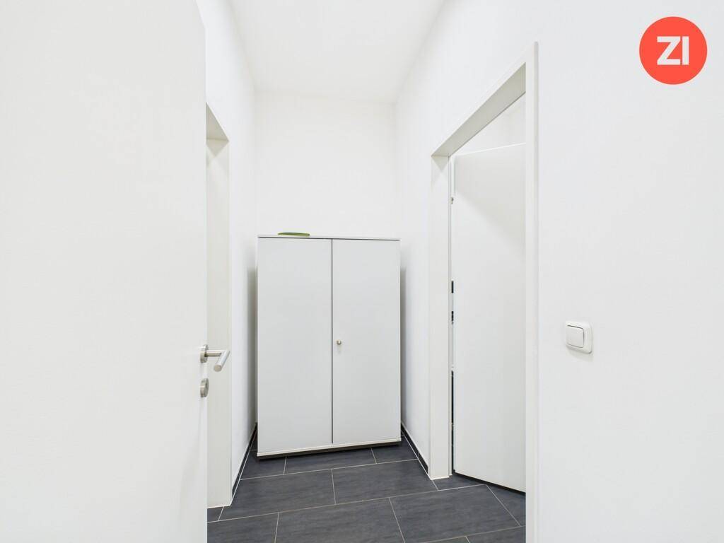Schmaler Flur mit dunklen Fliesen und einem praktischen weißen Schrank, der zusätzlichen Stauraum bietet.
