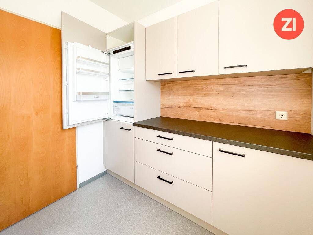 Helle Küchenzeile mit integriertem Kühlschrank, weißen Schränken und dunkler Arbeitsplatte.