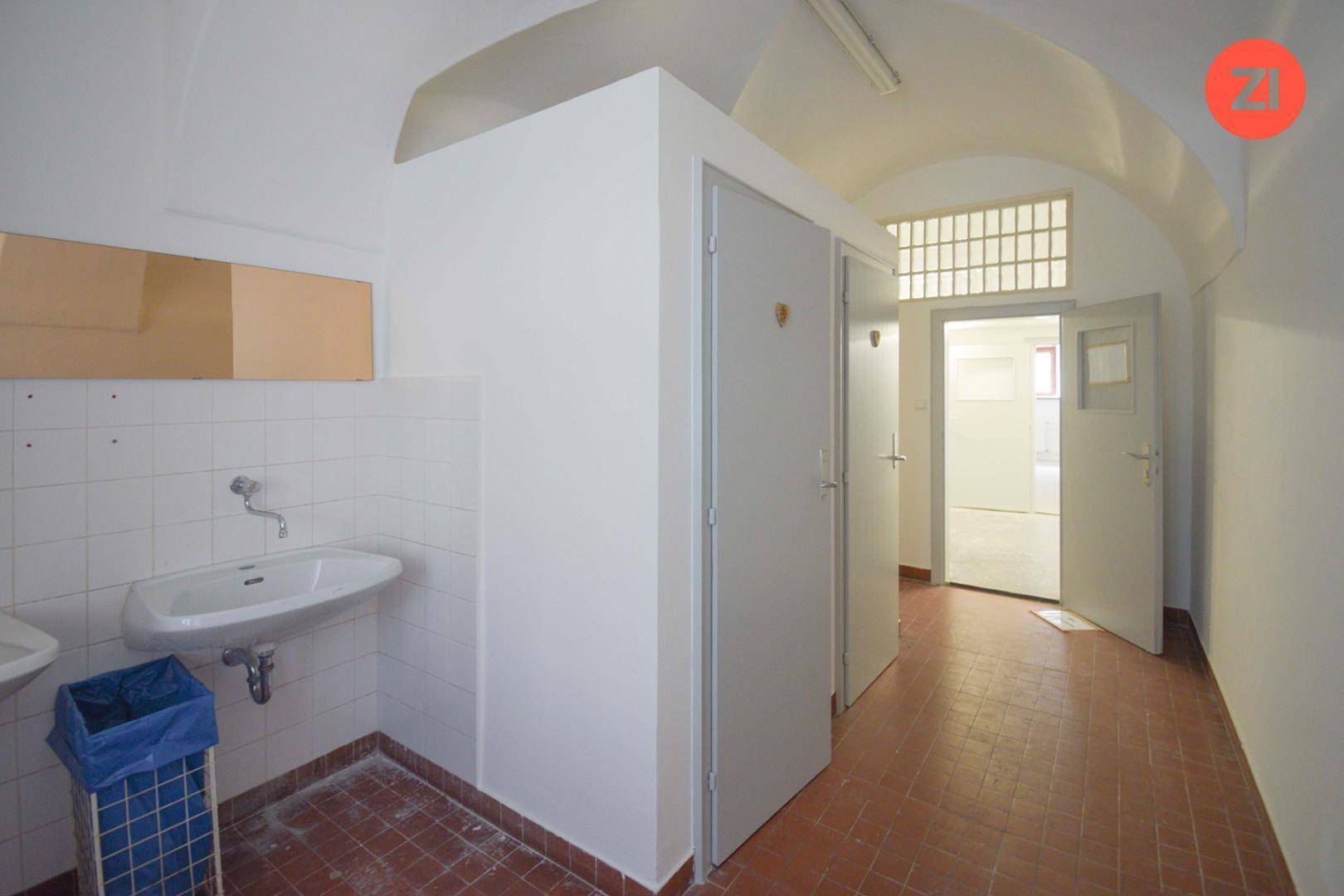 Sanitärbereich mit Waschbecken, weißen Fliesen und mehreren Toilettenkabinen, sauber und funktional.