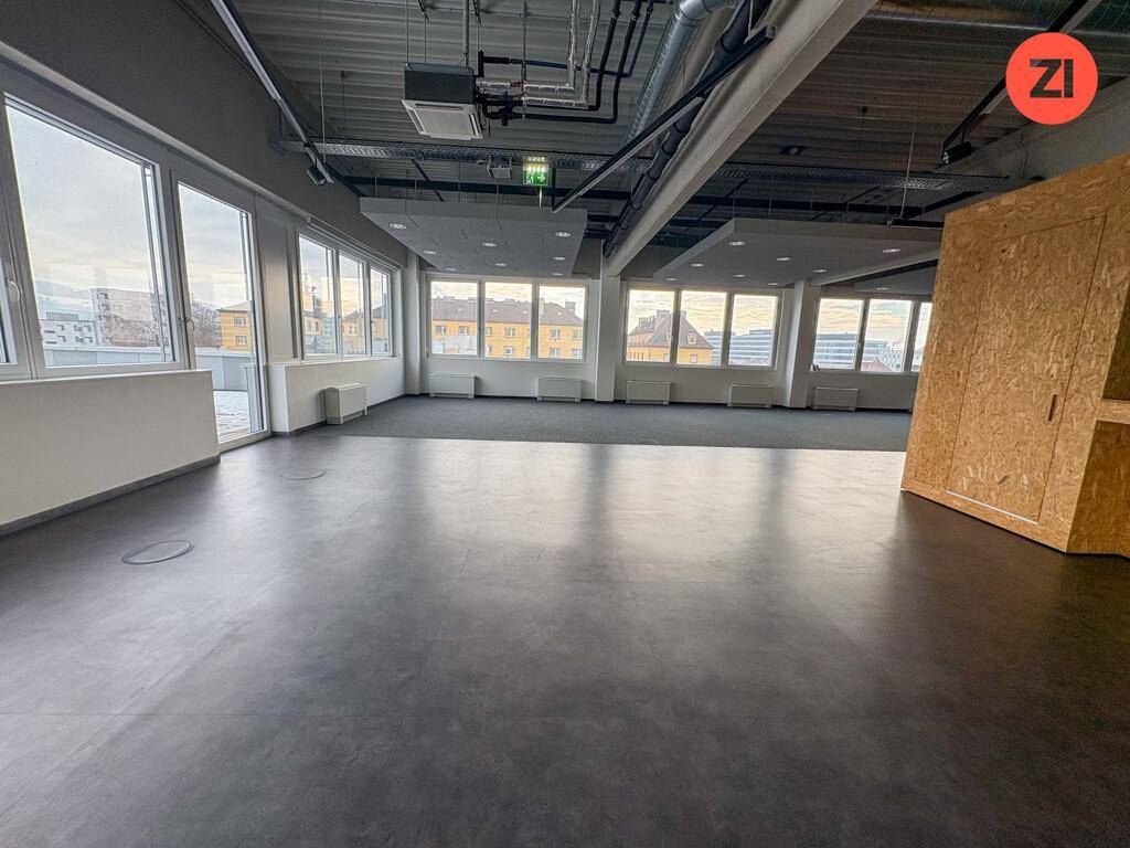 Weitläufiger Bürobereich mit Teppichboden, großen Fenstern und Blick auf die Stadt.
