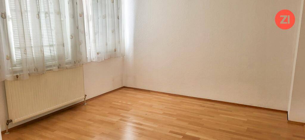 Leeres Zimmer mit hellem Holzfußboden und großen Fenstern, die für viel Helligkeit sorgen.