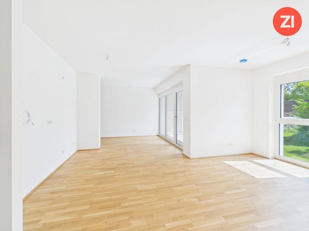 Heller, unmöblierter Wohnraum mit Parkettboden und großen Fenstern, die viel Licht spenden.