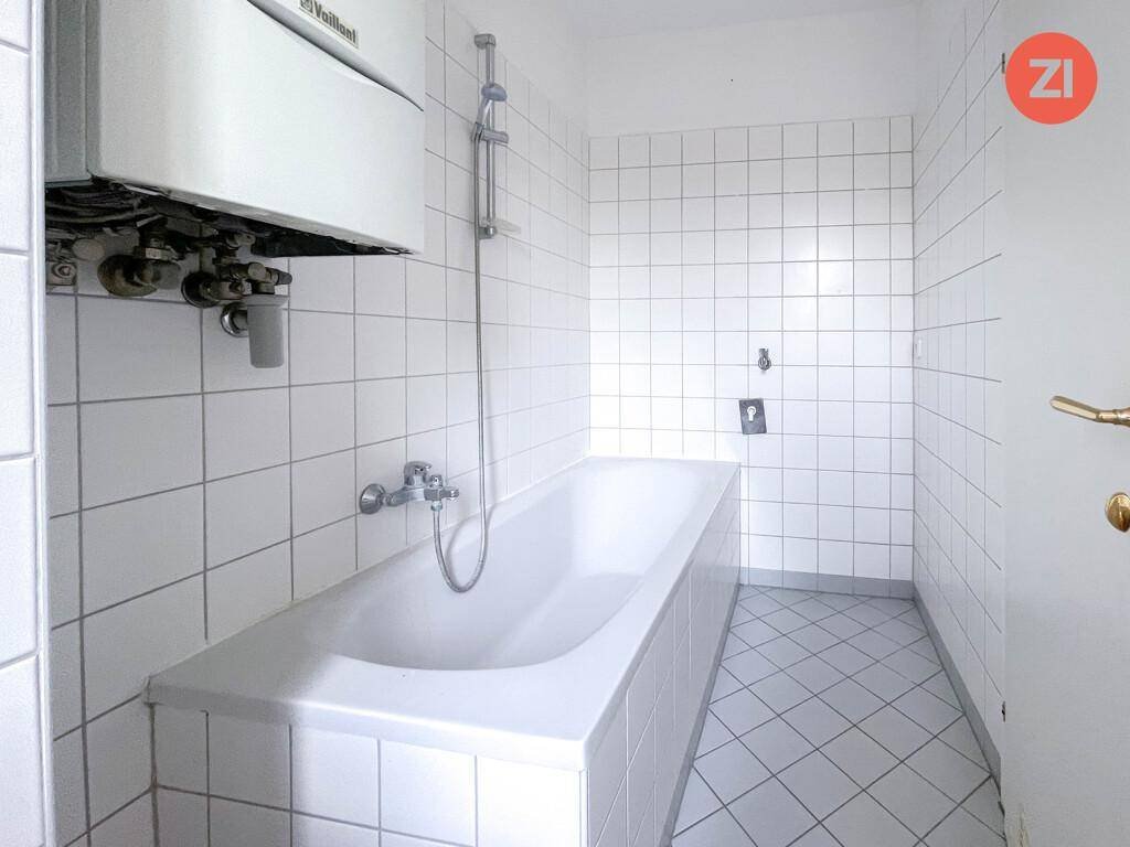 Gefliestes Badezimmer mit Badewanne und an der Wand montiertem Warmwasserbereiter.