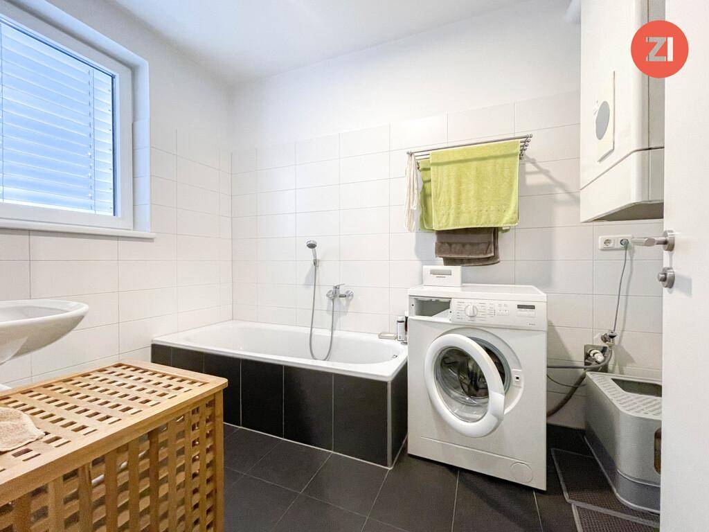 Badezimmer mit Badewanne, Waschmaschine, Fenster und weißen Fliesen.
