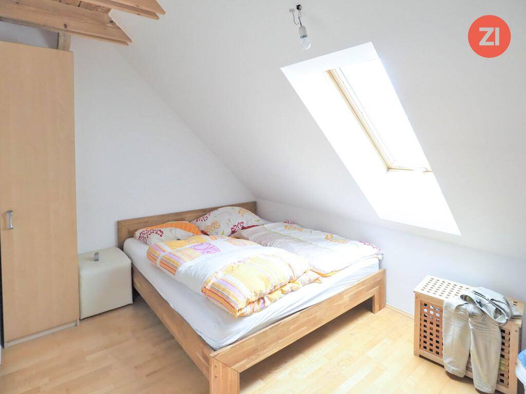 Helles Schlafzimmer im Dachgeschoss mit Holzbett, Dachfenster und schrägen Wänden.