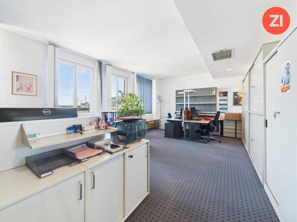 Großes Büro mit mehreren Arbeitsbereichen, Aktenschränken und Teppichboden, gut beleuchtet durch Fenster.