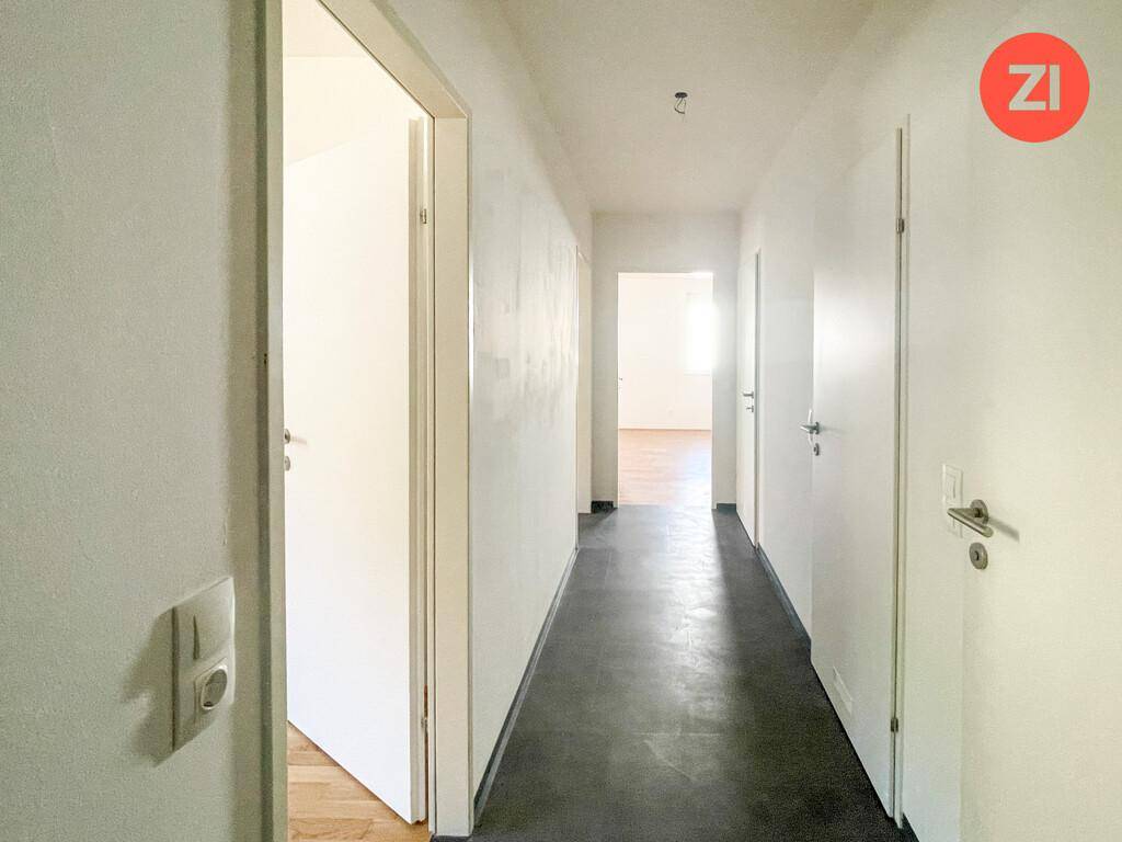 Langer, heller Flur mit dunklem Fliesenboden und mehreren Türen zu den Zimmern.