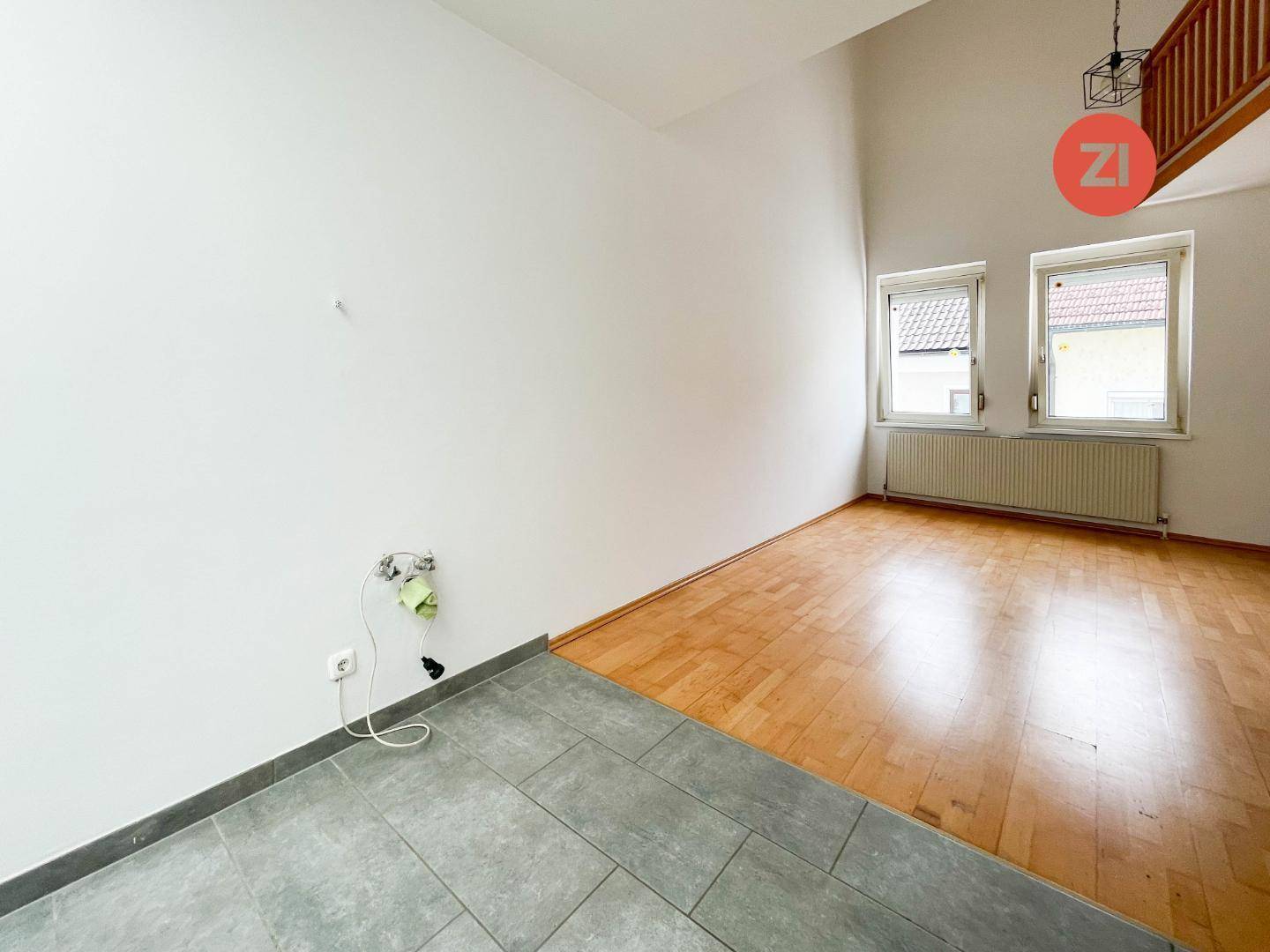 Heller Raum mit Holzboden und Fliesenbereich, vorbereitet für eine Küche.