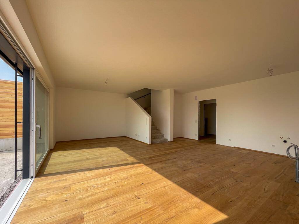 Großzügiger Wohnbereich mit Holzboden und breiter Schiebetür zur Terrasse.
