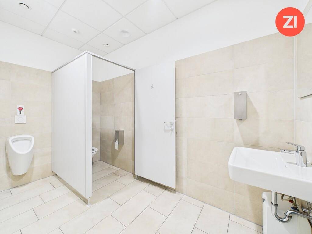 Moderne Toilettenanlage mit hellen Fliesen, Urinal und Waschbecken.