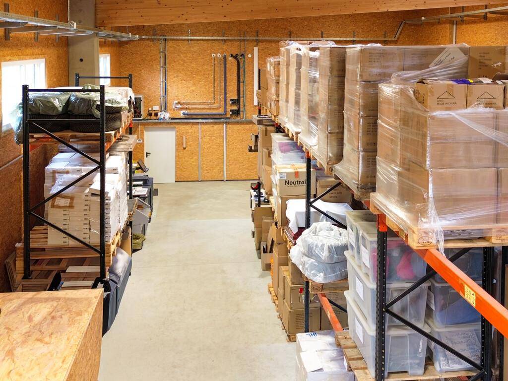 Gang in der Lagerhalle mit hohen Regalen auf beiden Seiten, gefüllt mit verpackten Gütern.