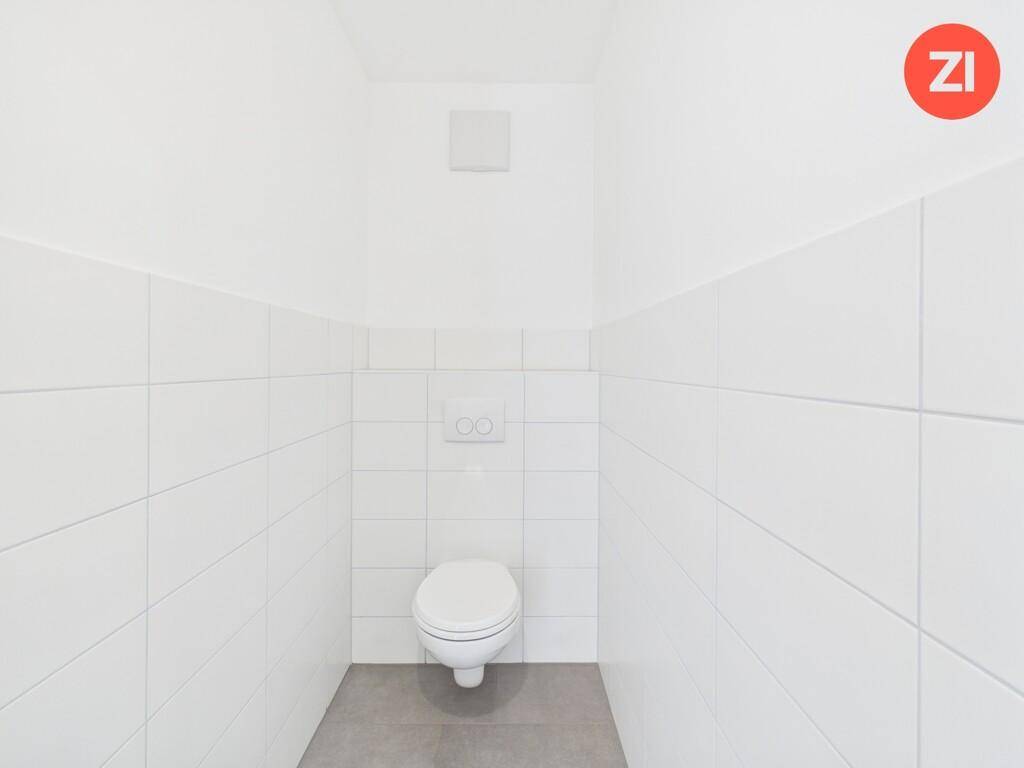 Separates WC mit wandhängender Toilette und weißen Fliesen, ausgestattet mit Abluftsystem.