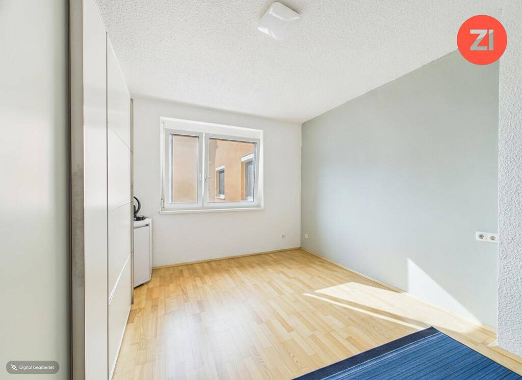 Helles Schlafzimmer mit Parkettboden, einer hellgrauen Akzentwand und Fenster.