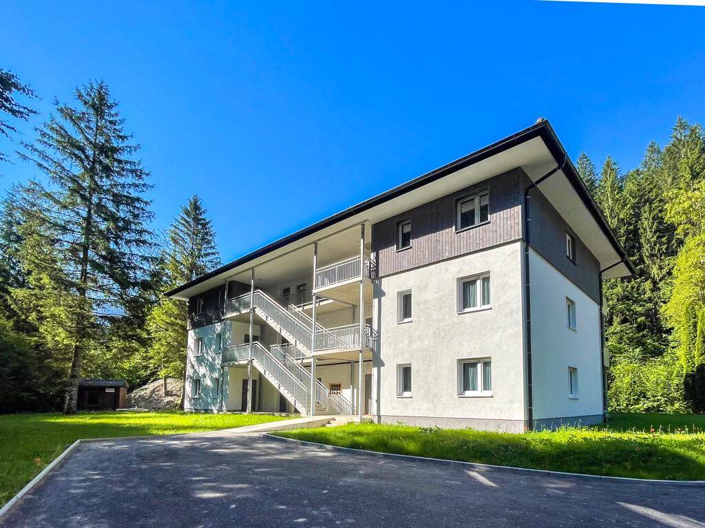 Modernes Mehrfamilienhaus mit Außentreppen und Balkonen, umgeben von viel Grün.