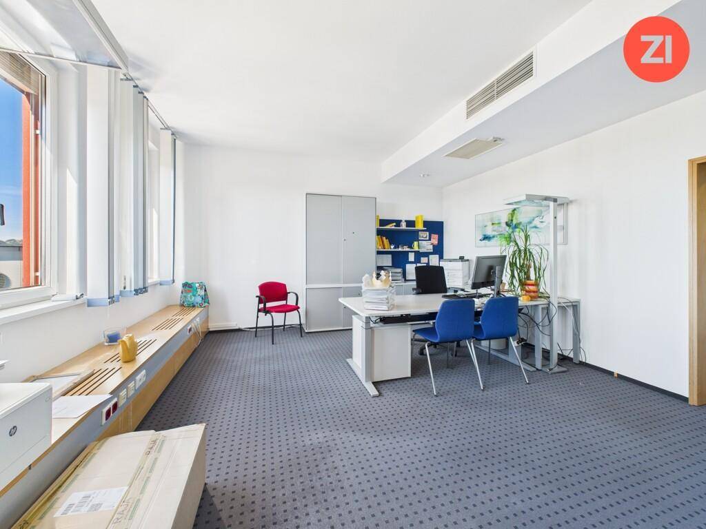 Einzelbüro mit Teppichboden, Schreibtisch und Fenstern, die einen Blick nach draußen ermöglichen.