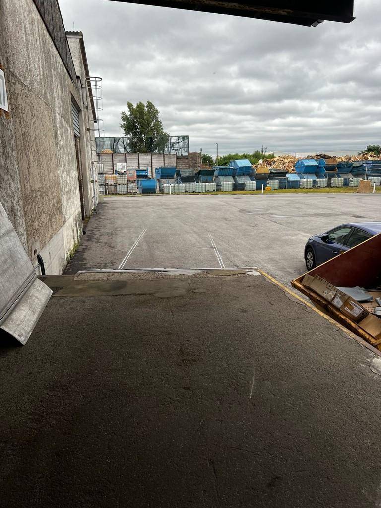 Außenbereich mit Laderampe, die zu einem Gebäude führt, und Lagercontainern im Hintergrund unter bewölktem Himmel.