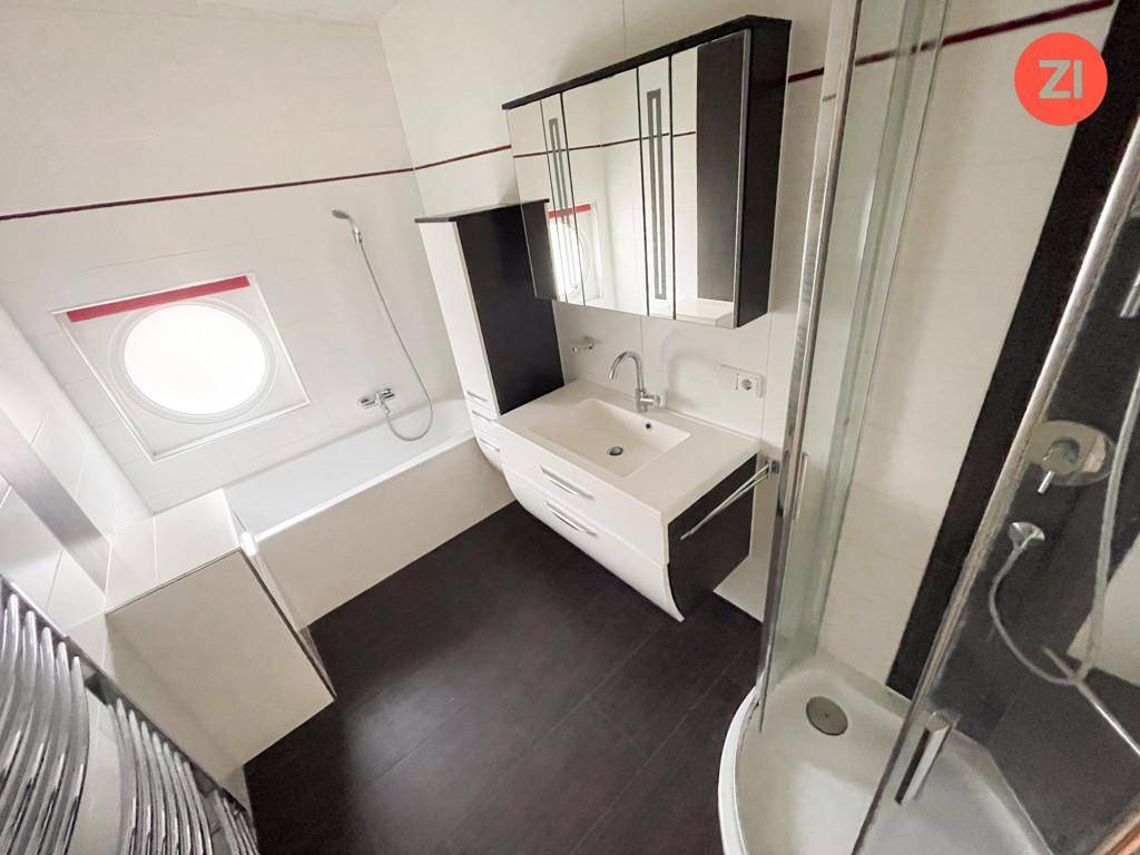 Modernes Badezimmer mit Badewanne, Dusche und einem runden Fenster für natürliches Licht.