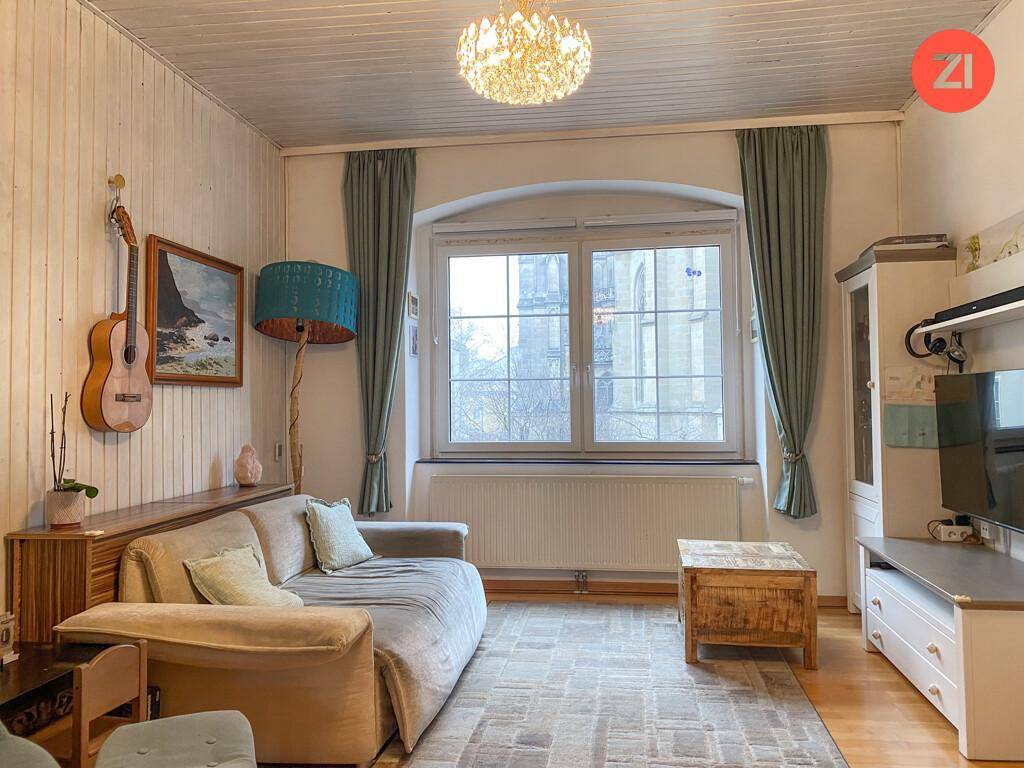 Gemütliches Wohnzimmer mit Holzwänden, beiger Couch und Blick auf ein historisches Gebäude.