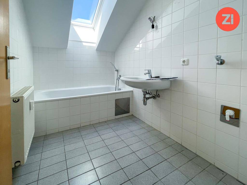 Badezimmer im Dachgeschoss mit Badewanne, Waschbecken, weißen Fliesen und einem Dachfenster.