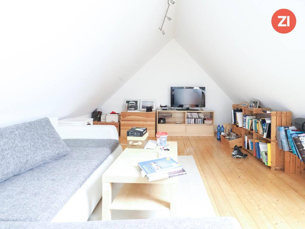 Gemütliches Wohnzimmer im Dachgeschoss mit Sofa, Fernseher und Bücherregalen.
