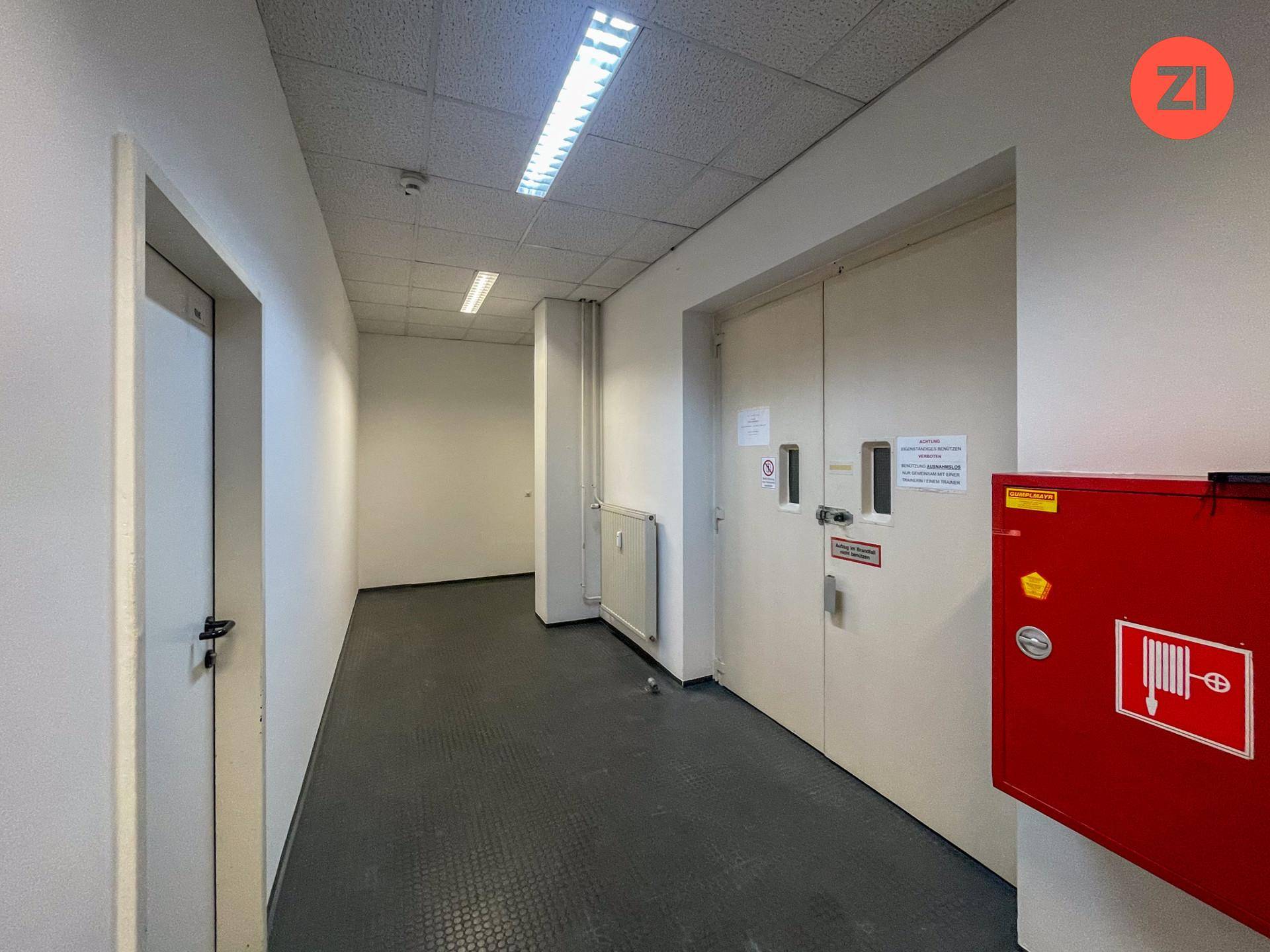 Langer Flur mit dunklem Boden, weißen Wänden und einem roten Brandschutzschrank.