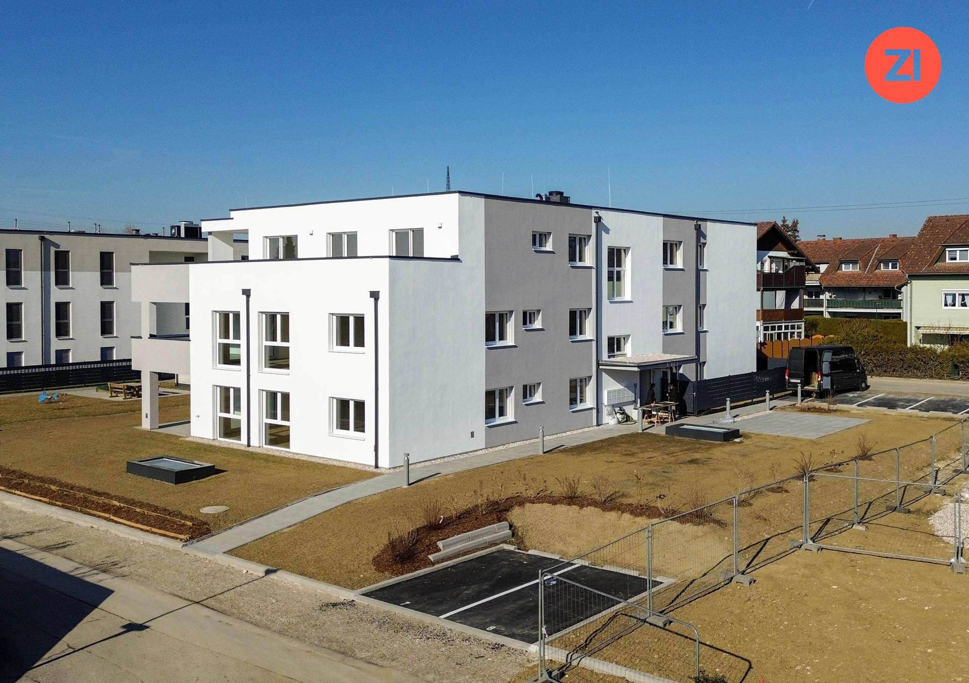 Moderne Wohnanlage mit weiß-grauer Fassade und Außenparkplätzen in sonniger Umgebung.
