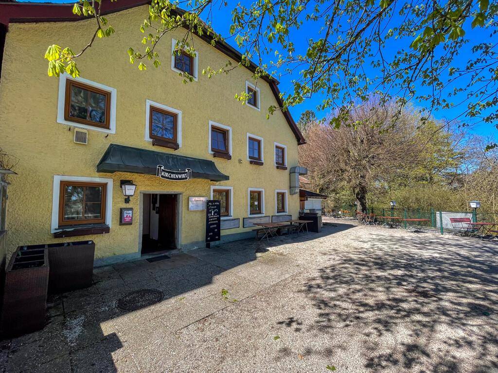 Fassade eines gelben Gasthauses mit braunen Fenstern und einem Außenbereich mit Tischen und Bänken.