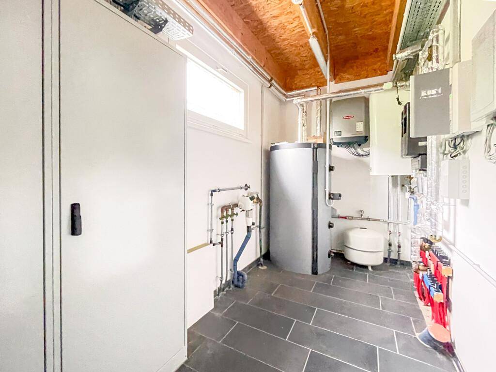 Technikraum mit Warmwasserspeicher, Heizungsanlagen und sichtbaren Installationen, gut organisiert.