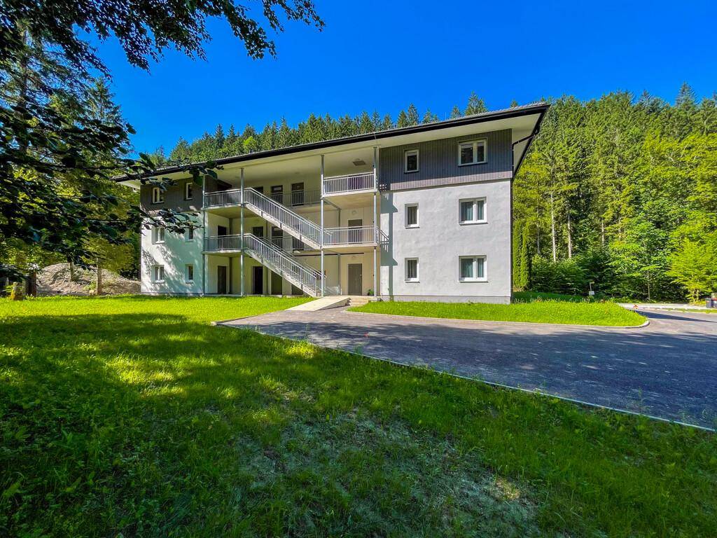 Modernes Mehrfamilienhaus mit Außentreppen und Balkonen, umgeben von Natur.