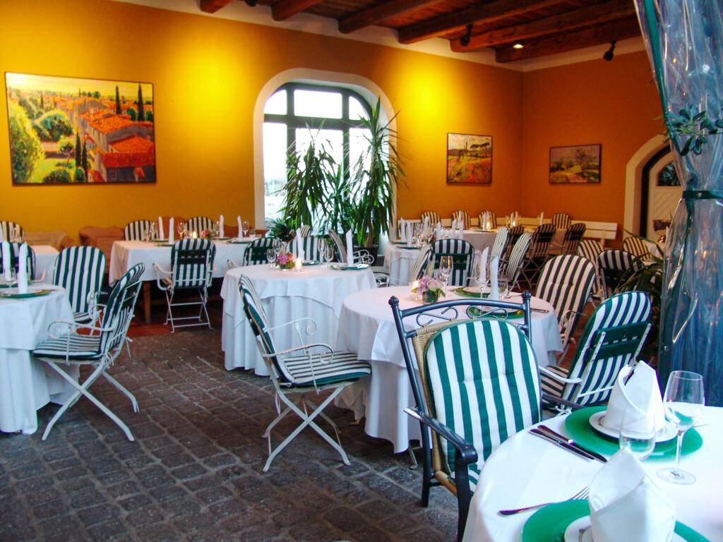Rustikaler Speisesaal mit gewölbten Fenstern, gedeckten Tischen und mediterranen Gemälden.