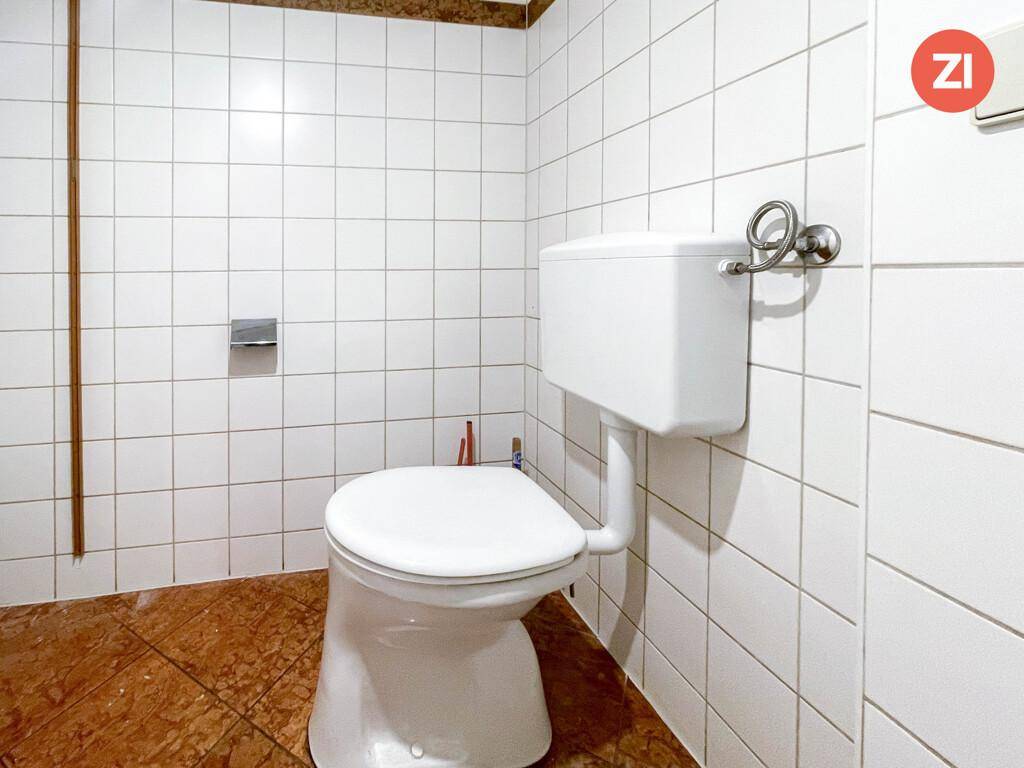 Einfache Toilette mit weißen Fliesen an den Wänden und Terrakottafliesen auf dem Boden.