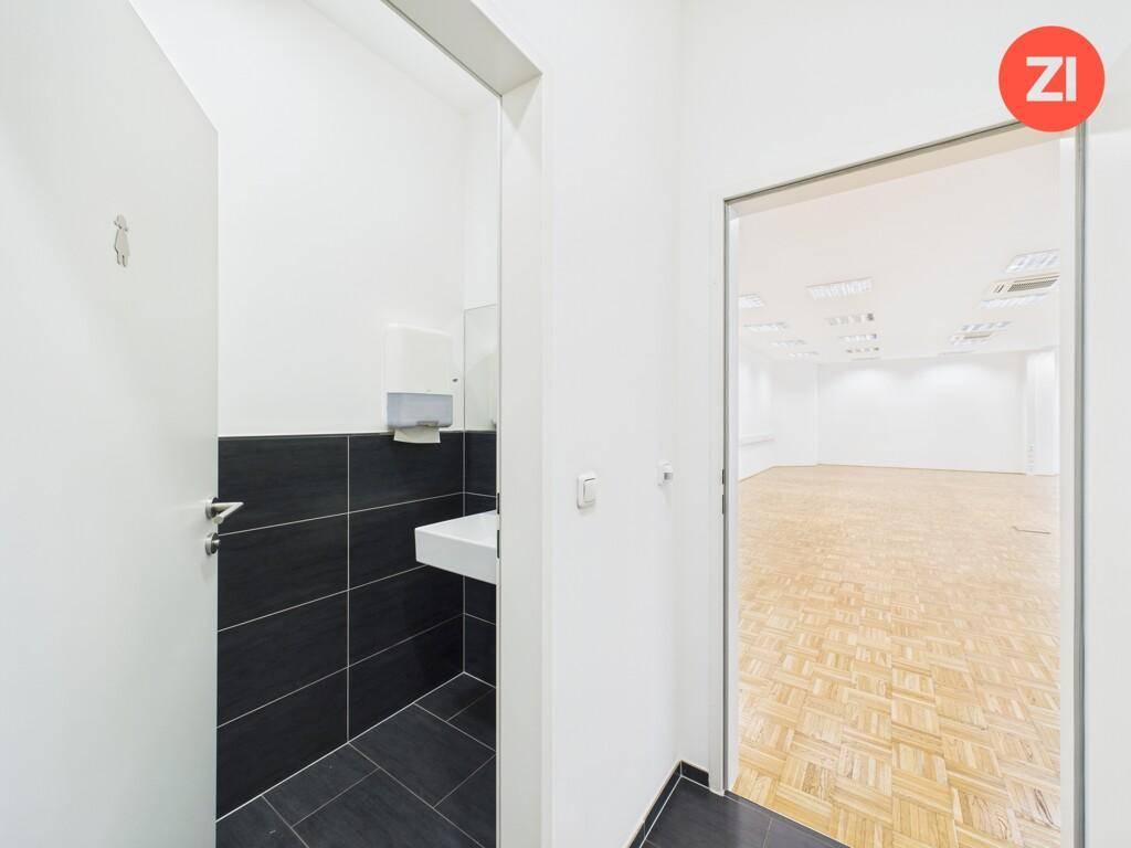 Modernes WC mit dunklen Fliesen, einem Waschbecken und Blick in den angrenzenden Bürobereich.