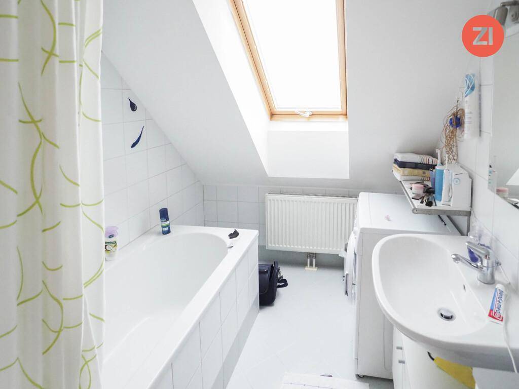 Helles Badezimmer im Dachgeschoss mit Badewanne, Waschbecken und Dachfenster.